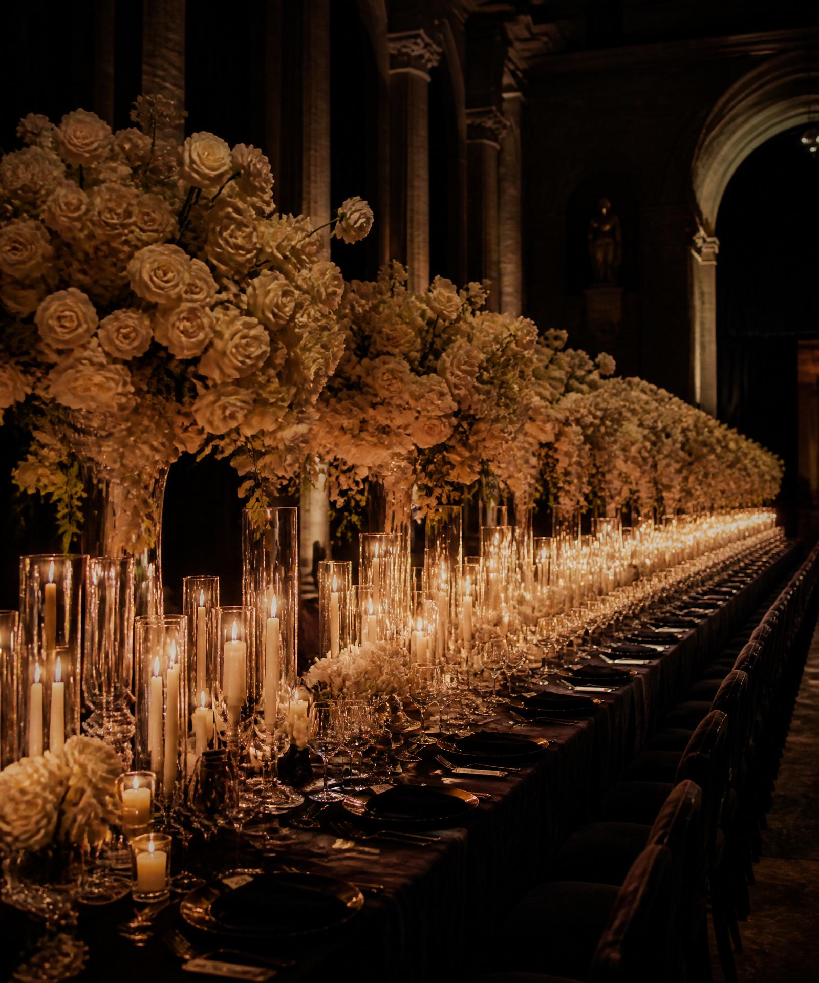 Long luxury candlelit banquet table with ivory floral installations in a cathedral hall